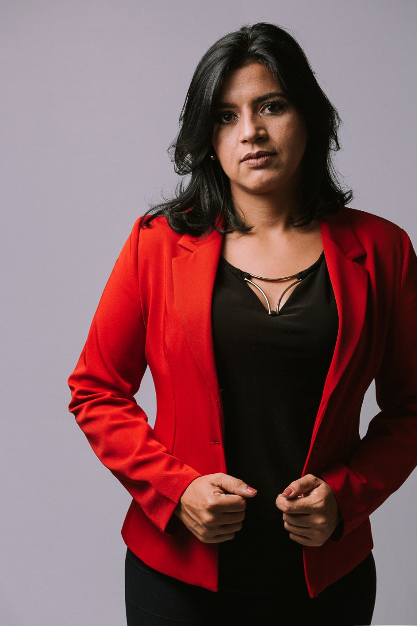 Larissa Duarte, de blazer vermelho, olhando para frente