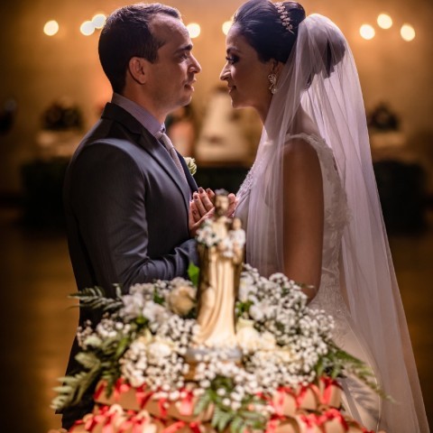 Um casal de noivos de frente um pro outro num altar, de lado para a camera